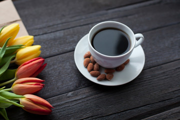 Fototapeta na wymiar white cup of coffee with yellow and orange tulip on black wood background