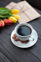 white cup of coffee with yellow and orange tulip on black wood background