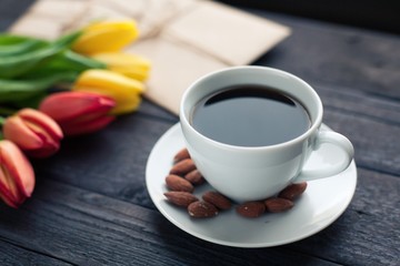 white cup of coffee with yellow and orange tulip on black wood background