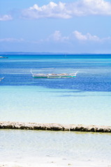 Obraz premium White fishing boat anchored in clear blue water on white sand beach