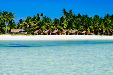 Beautiful white coral sand beach with palms and cottages, turquoise blue ocean
