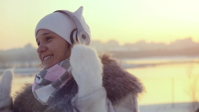 Winter beautiful girl in winter clothes dancing with headphones enjoying outdoors during sunset in slow motion. 1920x1080