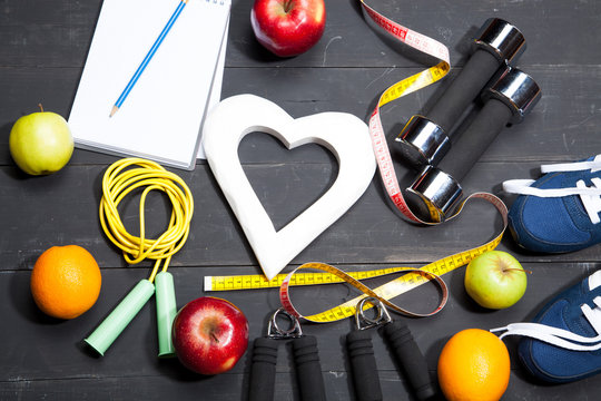 Heart, fruit and dumbbells. Fitness, healthy lifestyle on a black wooden background