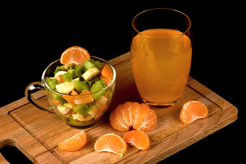 Fruit salad, segments of tangerine and glass with drink on a black background.
