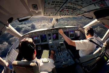 Flight Deck of modern passenger jet aircraft. Pilots at work. Cloudy sky and sunset view from the airplane cockpit. - obrazy, fototapety, plakaty