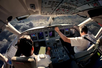 Tuinposter Flight Deck of modern passenger jet aircraft. Pilots at work. Cloudy sky and sunset view from the airplane cockpit. © petrovalexey