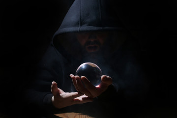 man in a black hood with cristal ball