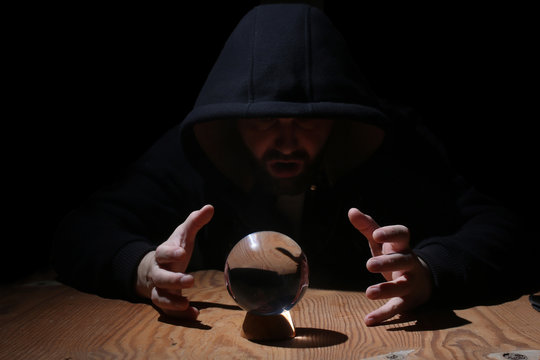 man in a black hood with cristal ball