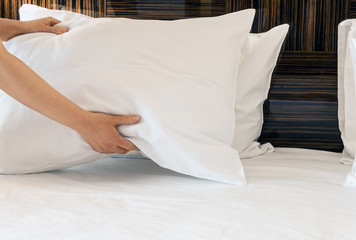 female hands corrected pillow on the bed. Concept on preparation of bed in a hotel room or at home