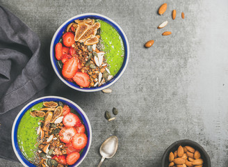 Healthy breakfast. Green smoothie bowls with strawberries, granola, chia and pumpkin seeds, dried figs and nut over grey concrete background, top view, copy space. Diet, clean eating food concept