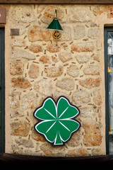Neon sign 4-sheeted clover, on a stone wall under a green lamp. Irlansky pub