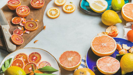 Natural fresh citrus fruits in ceramic plates and wooden rustic board over grey marble table background, selective focus, copy space