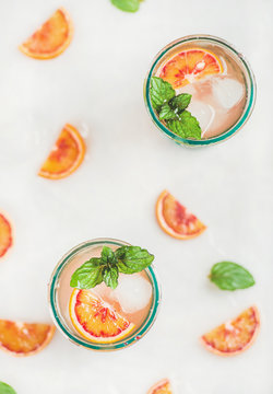 Blood orange fresh summer homemade lemonade with ice and mint in glasses, light grey marble background, top view, selective focus, vertical composition