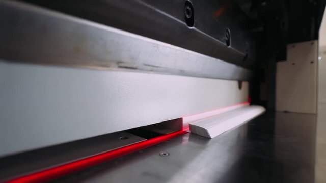 Paper cutting process, close-up, paper cutting machine cuts sheets of paper, red laser.
