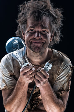 Portrait of burnt man with light bulb and electric plug over black background. Young man with dirty burnt face in funny sad expression in electricity DIY has a electric shock. 