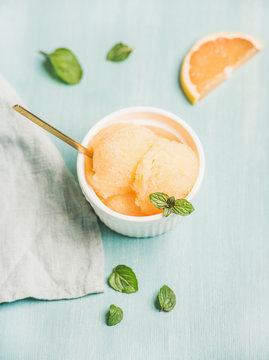 Pink grapefruit sorbet with fresh mint leaves in white bowl over blue painted background, selective focus. Fresh healthy raw vegan summer dessert concept