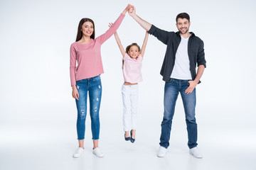 Obraz premium Happy little girl hanging on parents hands on white