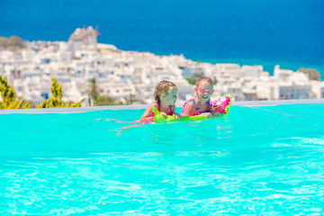 Adorable little girls playing in outdoor swimming pool with beautiful view