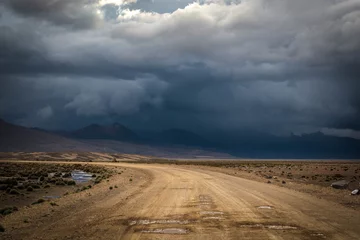 Poster Landscape with dirt road in the mountains under stormy sky.Rural mountain road in Peru, South America, just before the snow storm. Mountains in the background. © skinfaxi
