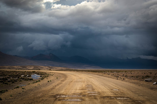 Landscape with dirt road in the mountains under stormy sky.Rural mountain road in Peru, South America, just before the snow storm. Mountains in the background. © skinfaxi