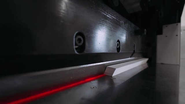 Paper cutting process, close-up, paper cutting machine cuts sheets of paper, red laser.
