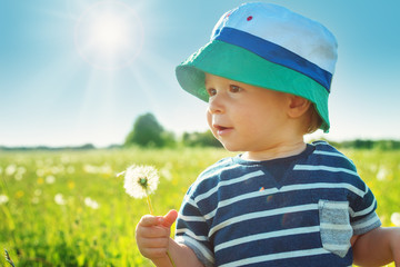 Baby boy standing in grass on the fieald with dandelions