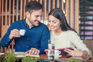 Young couple drinking coffee and reading a book in the cafe. Education, dating, relationships, love concept