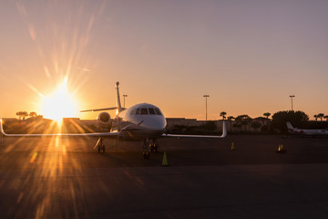 Naklejka na ściany i meble Modern Jet parked on runway in sunny day, amazing sunset.
