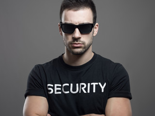 Dramatic portrait of tough macho security guard man with crossed arms over dark gray studio...