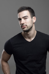 Fototapeta premium Confident macho athletic man wearing black t-shirt looking at camera suspiciously over dark gray studio background.