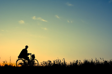 Fototapeta na wymiar Silhouette of man and old bicycle on grass with the sky sunset, color of vintage tone and soft focus concept journey