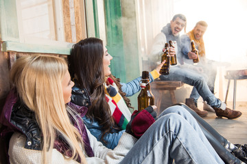 Side view of cheerful friends drinking beer on porch