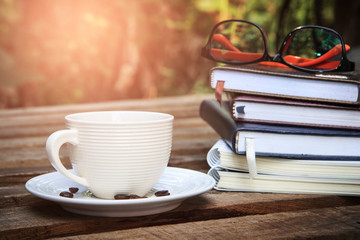 eyeglasses on book with hot coffee cup on nature background, vintage filter. learning concept and reading.