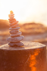 Tall Stack of Stones / Tower of pebbles with shell on top at bright evening sunshine, built on wooden groin