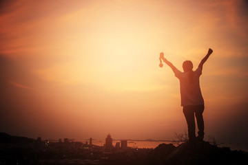 Silhouette woman raising hands and holding gold medal looking the city with sunset sky. victory concept. business success.