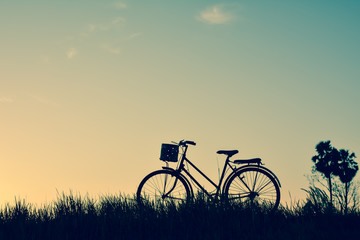 Fototapeta na wymiar Silhouette of old bicycle on grass with the sky sunset, color of vintage tone and soft focus concept journey