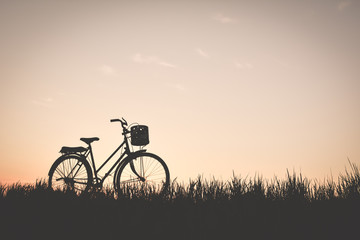 Obraz premium Silhouette of old bicycle on grass with the sky sunset, color of vintage tone and soft focus concept journey