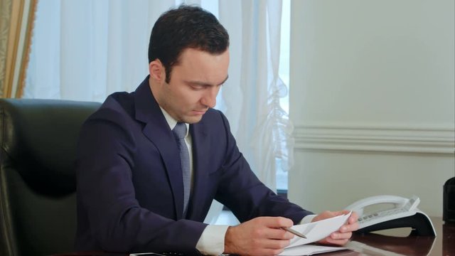 Young businessman reading paperwork at desk in office and smiling