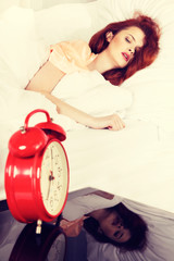 Sleeping woman with her hand touching alarm clock on bed