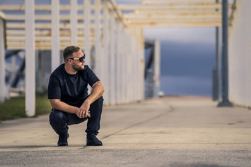 Conceptual photo of young and serious rapper in black zipped jacket and sunglasses in front of the wall. He is looking forward at something. Barcelona, Spain.