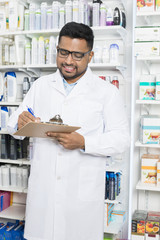 Smiling Chemist Writing On Clipboard In Pharmacy