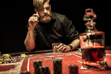 Handsome bearded man smoking cigar and drinking whisky while playing poker