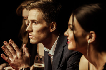 Side view of elegant young people drinking alcohol and looking away on black