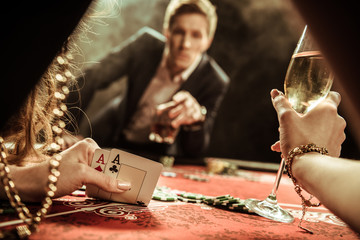 partial view of woman with drink looking at cards while playing poker