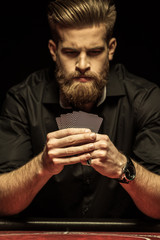 Serious bearded man holding poker cards on black