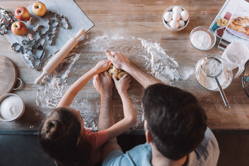 'Overhead view of father and daughter kneading dough at kitchen table
