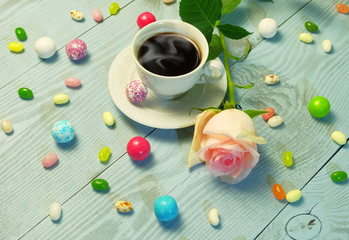 Fototapeta na wymiar A cup of coffee, colorful candies and jelly beans and a rose on a blue wooden table.