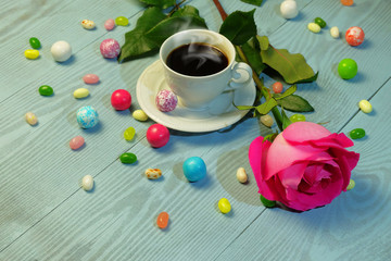 Obraz na płótnie Canvas A cup of coffee, colorful candies and jelly beans and a rose on a blue wooden table.