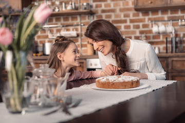 'portrait of cheerful mother and daughter with cake on table, mother's day holiday concept