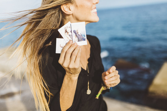 Young woman showing instant photos of herself at the seafront